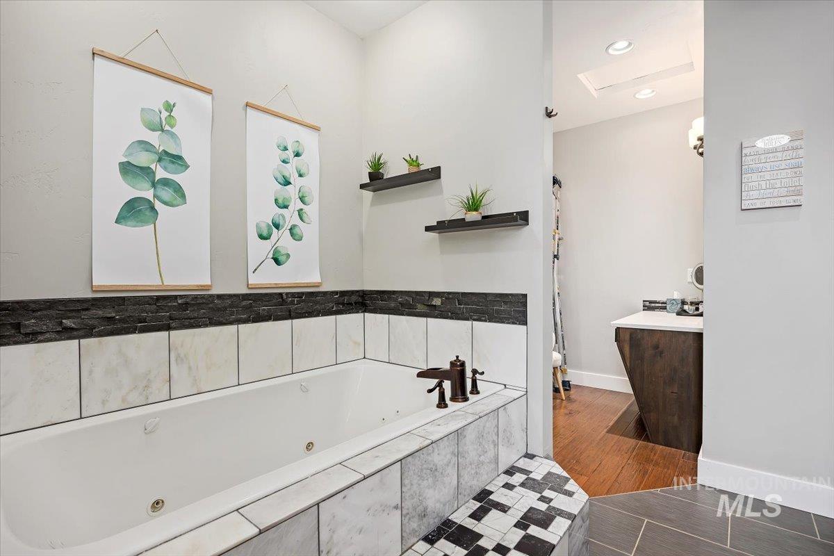 Bathroom featuring a jetted tub, vanity, dark tile patterned floors, and recessed lighting