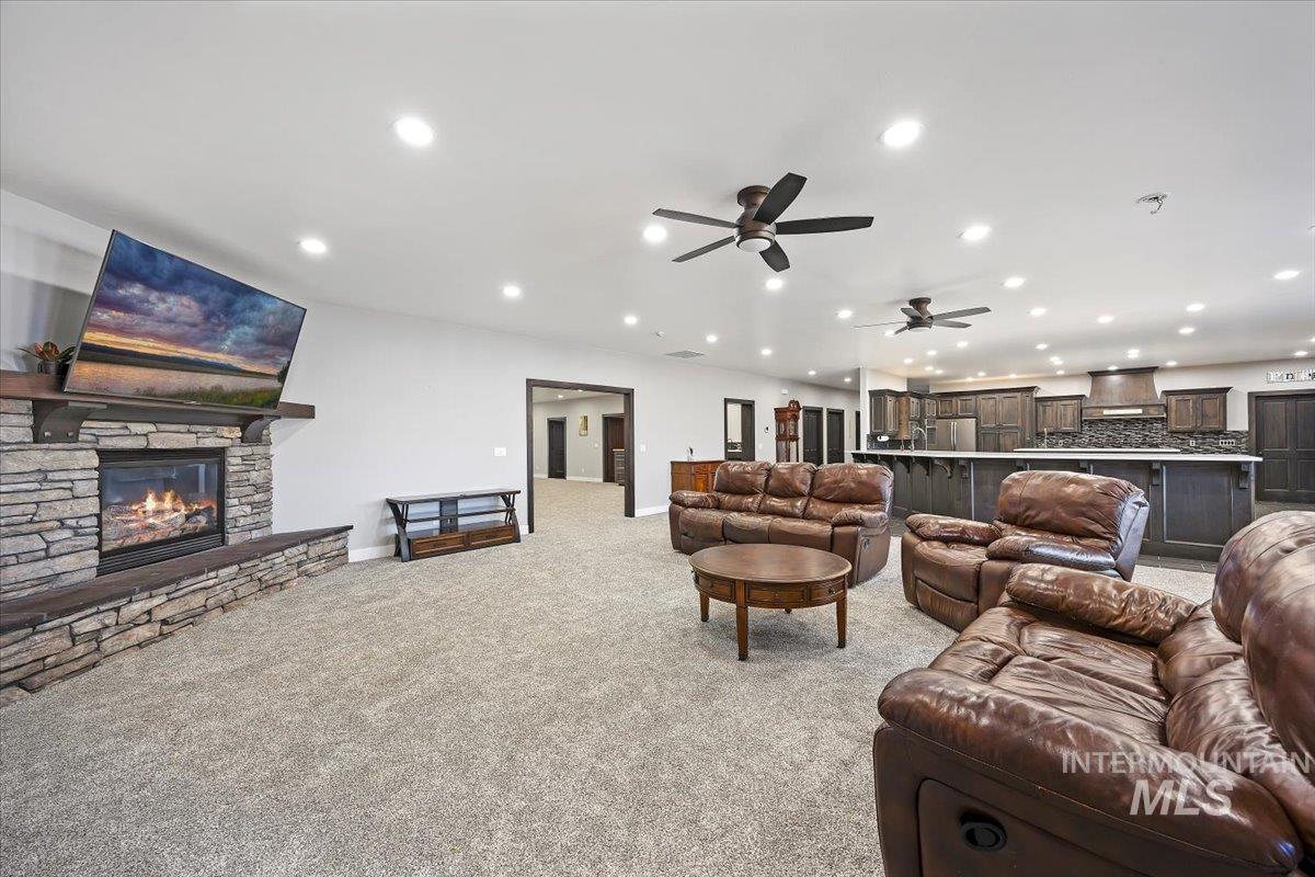 Living area featuring light carpet, recessed lighting, a stone fireplace, and a ceiling fan