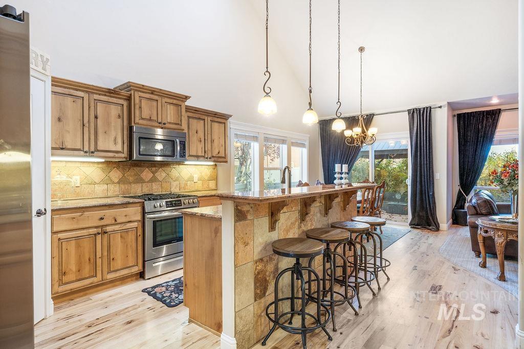 Kitchen with a breakfast bar area, high vaulted ceiling, appliances with stainless steel finishes, decorative light fixtures, and light wood-style floors