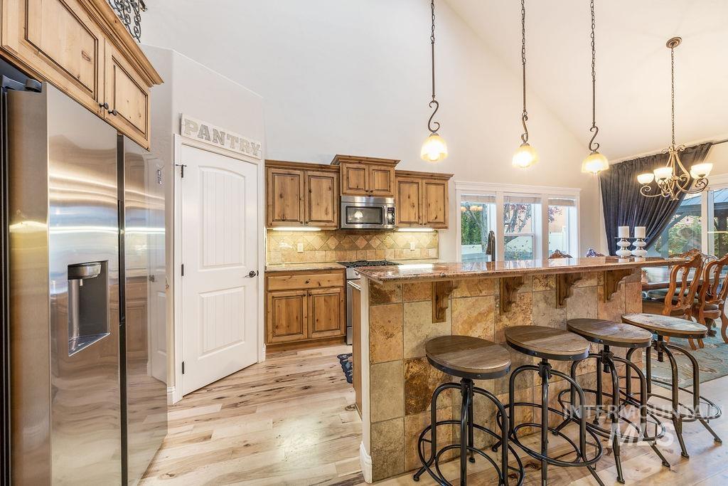 Kitchen featuring a breakfast bar area, appliances with stainless steel finishes, high vaulted ceiling, decorative light fixtures, and brown cabinetry