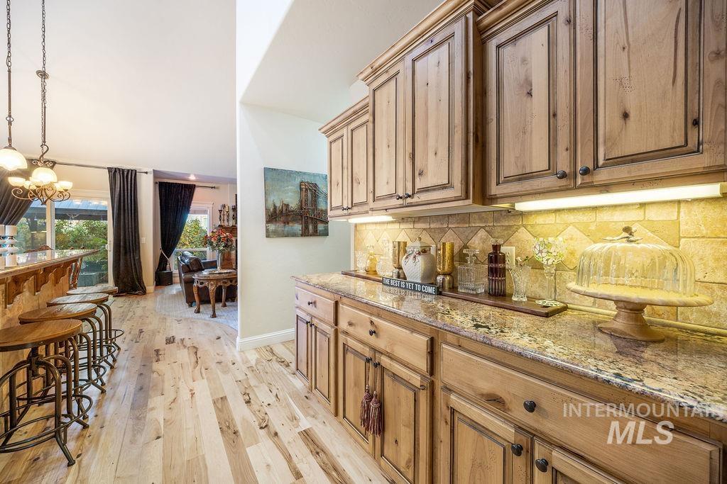 Bar with light stone counters, pendant lighting, light wood-style flooring, decorative backsplash, and a chandelier