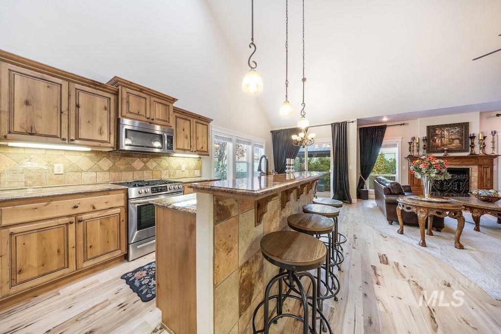 Kitchen with a kitchen bar, appliances with stainless steel finishes, decorative light fixtures, high vaulted ceiling, and a fireplace