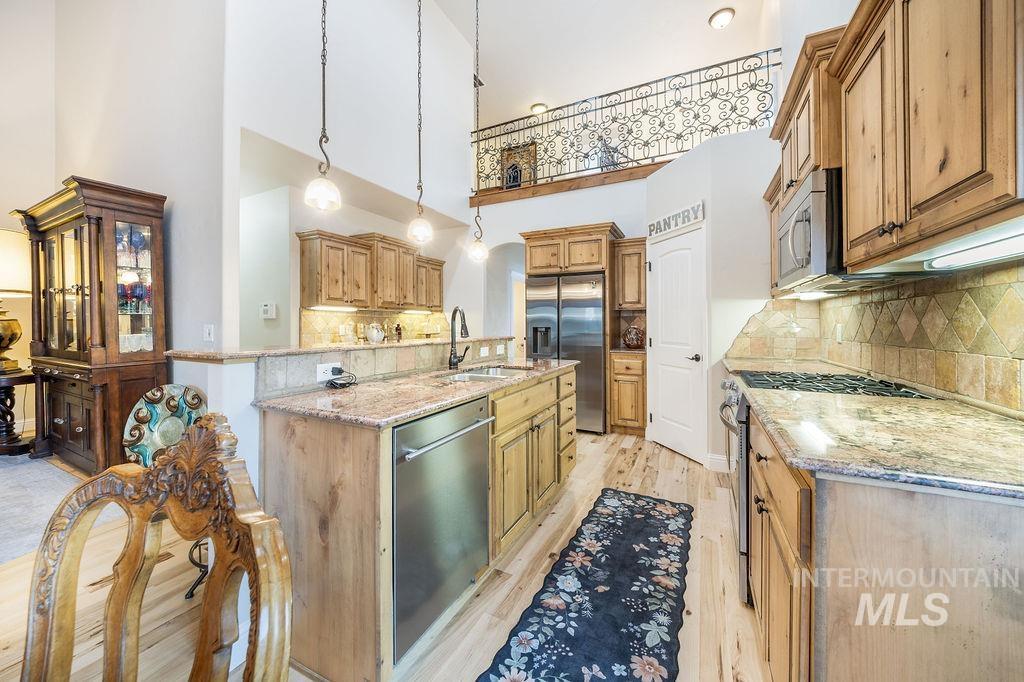 Kitchen with light stone countertops, decorative backsplash, stainless steel appliances, hanging light fixtures, and a towering ceiling
