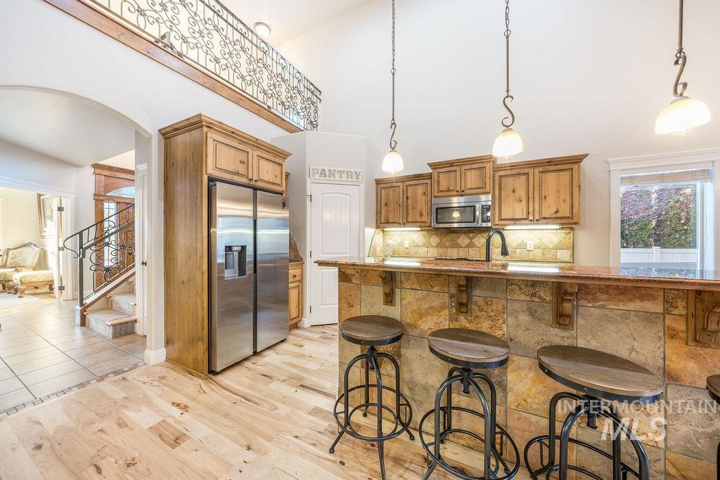 Kitchen with arched walkways, appliances with stainless steel finishes, pendant lighting, a kitchen breakfast bar, and brown cabinetry