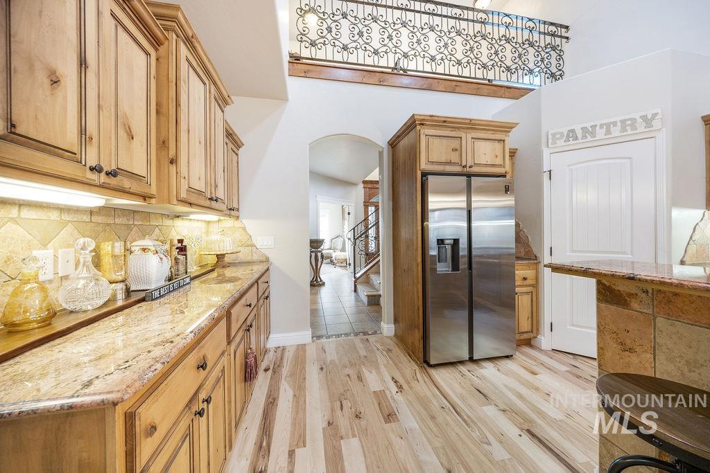 Kitchen with arched walkways, stainless steel fridge with ice dispenser, light stone countertops, light wood finished floors, and decorative backsplash