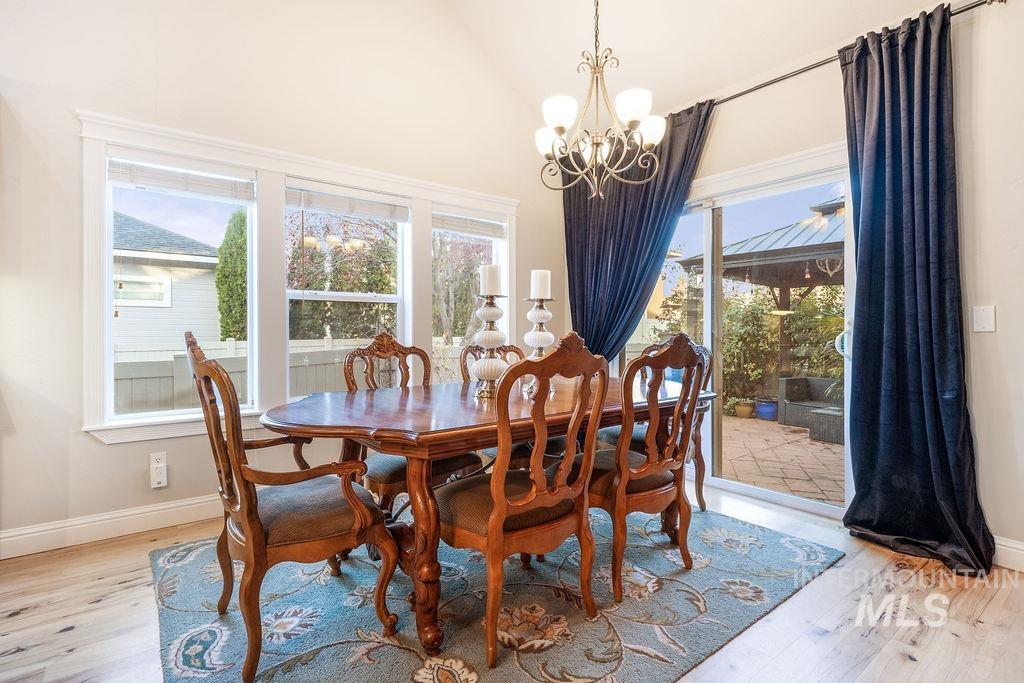 Dining room with healthy amount of natural light, light wood finished floors, vaulted ceiling, and a chandelier