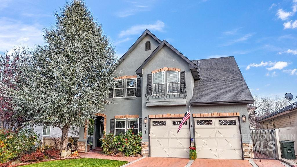 View of front of property featuring stone siding, a garage, stucco siding, and roof with shingles