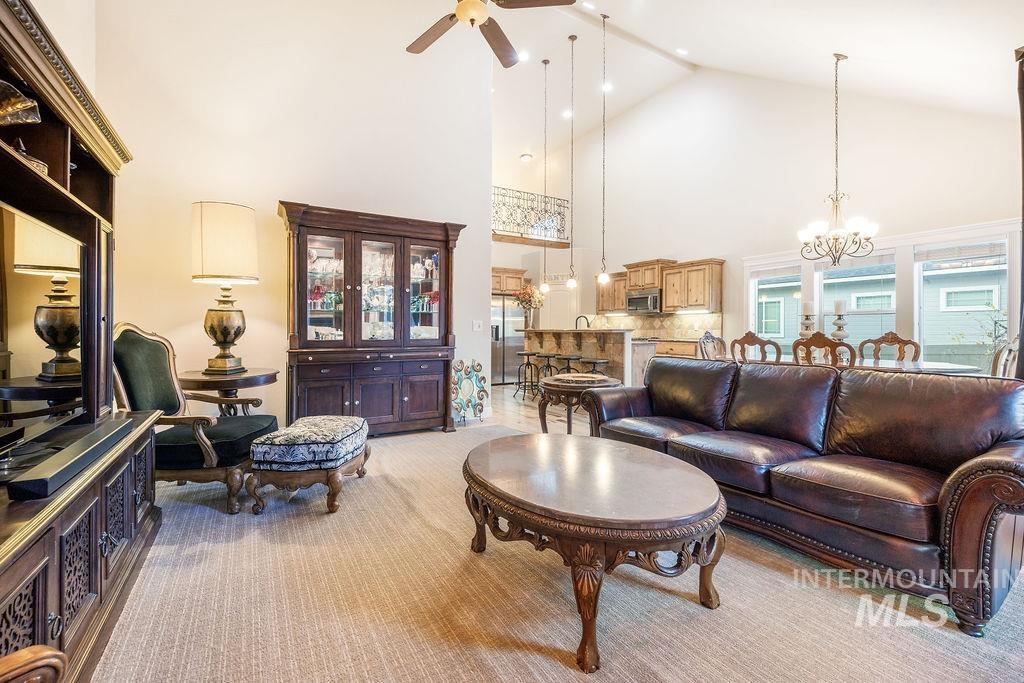 Living area featuring a chandelier, high vaulted ceiling, a ceiling fan, and light colored carpet
