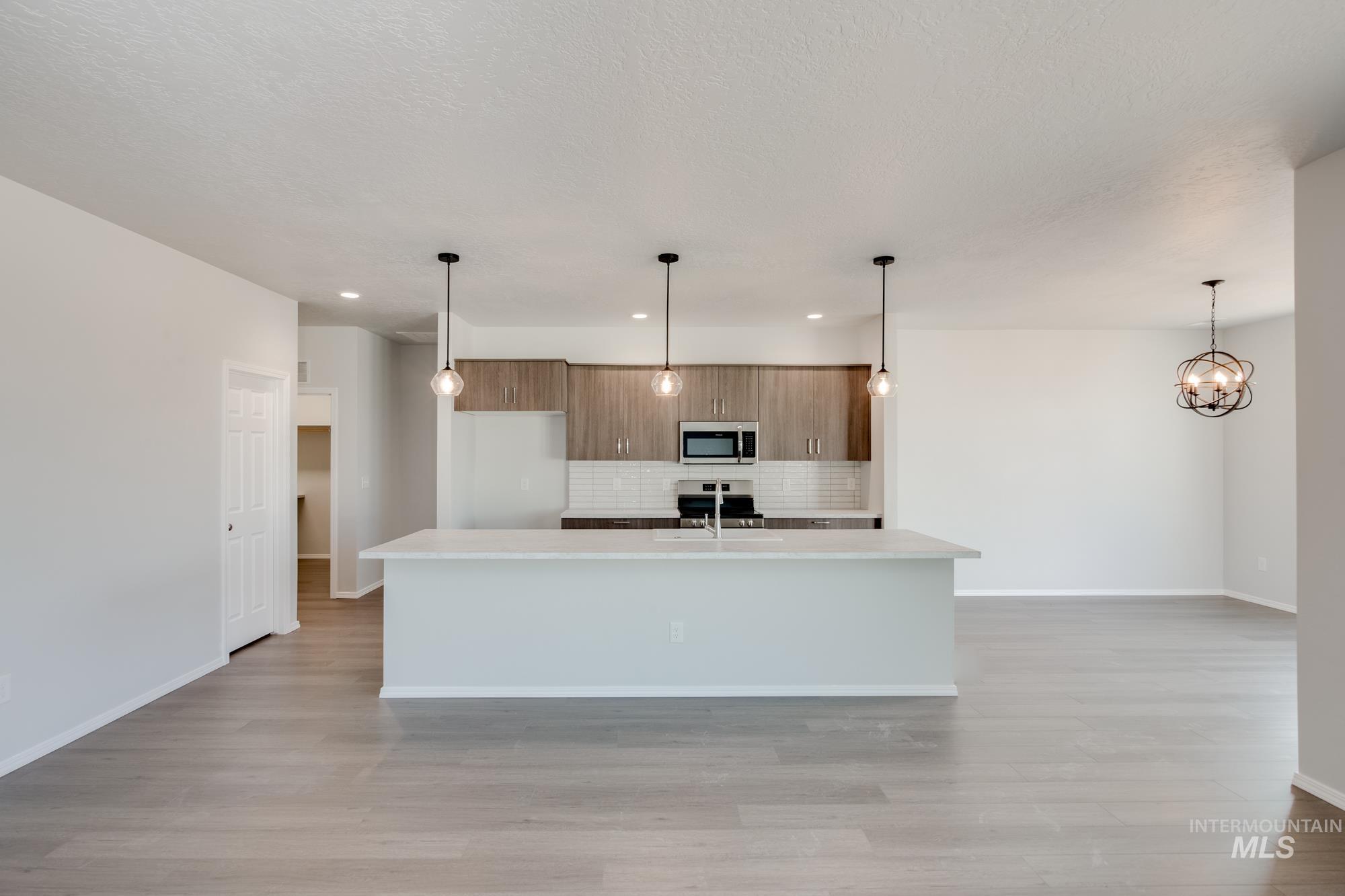 Kitchen featuring decorative light fixtures, decorative backsplash, brown cabinets, a kitchen island with sink, and light wood finished floors