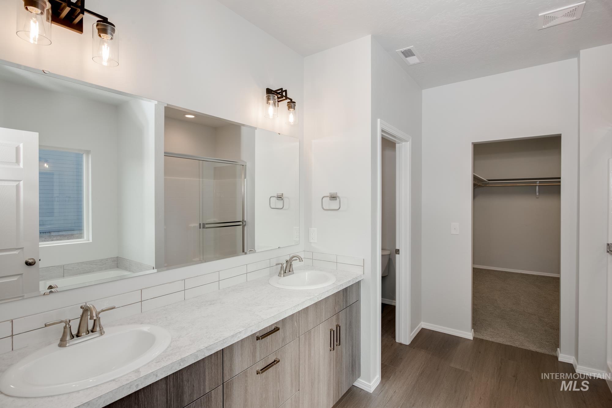 Bathroom featuring a walk in closet, a stall shower, dark wood-style floors, double vanity, and a bath