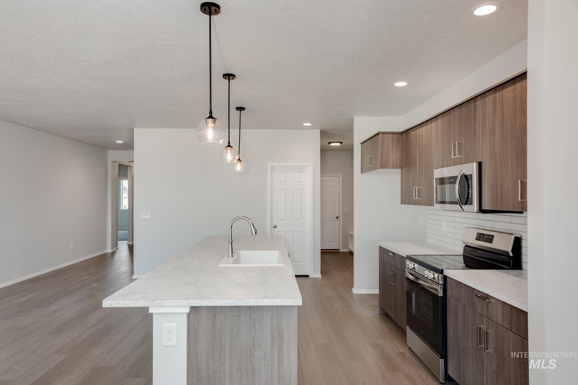 Kitchen with appliances with stainless steel finishes, modern cabinets, light countertops, decorative light fixtures, and light wood-style flooring