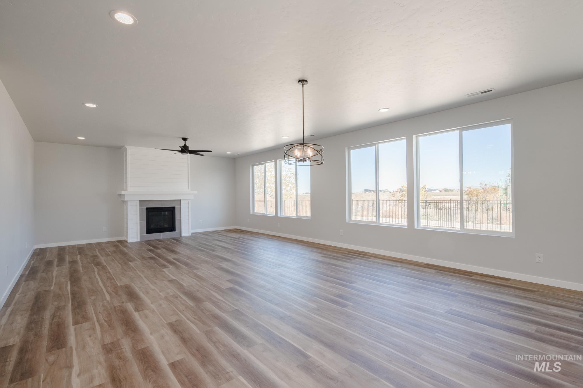 Unfurnished living room with light wood-style flooring, a fireplace, recessed lighting, ceiling fan, and a chandelier