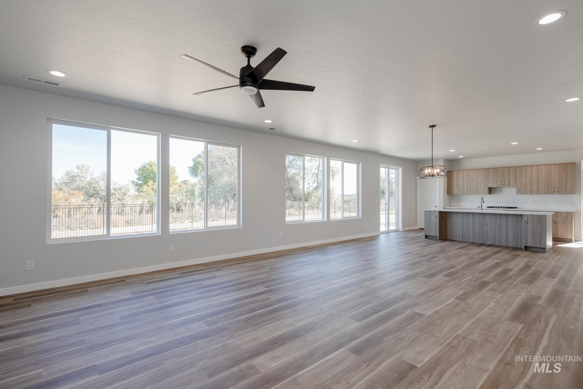 Unfurnished living room with dark wood finished floors, recessed lighting, a ceiling fan, and a chandelier