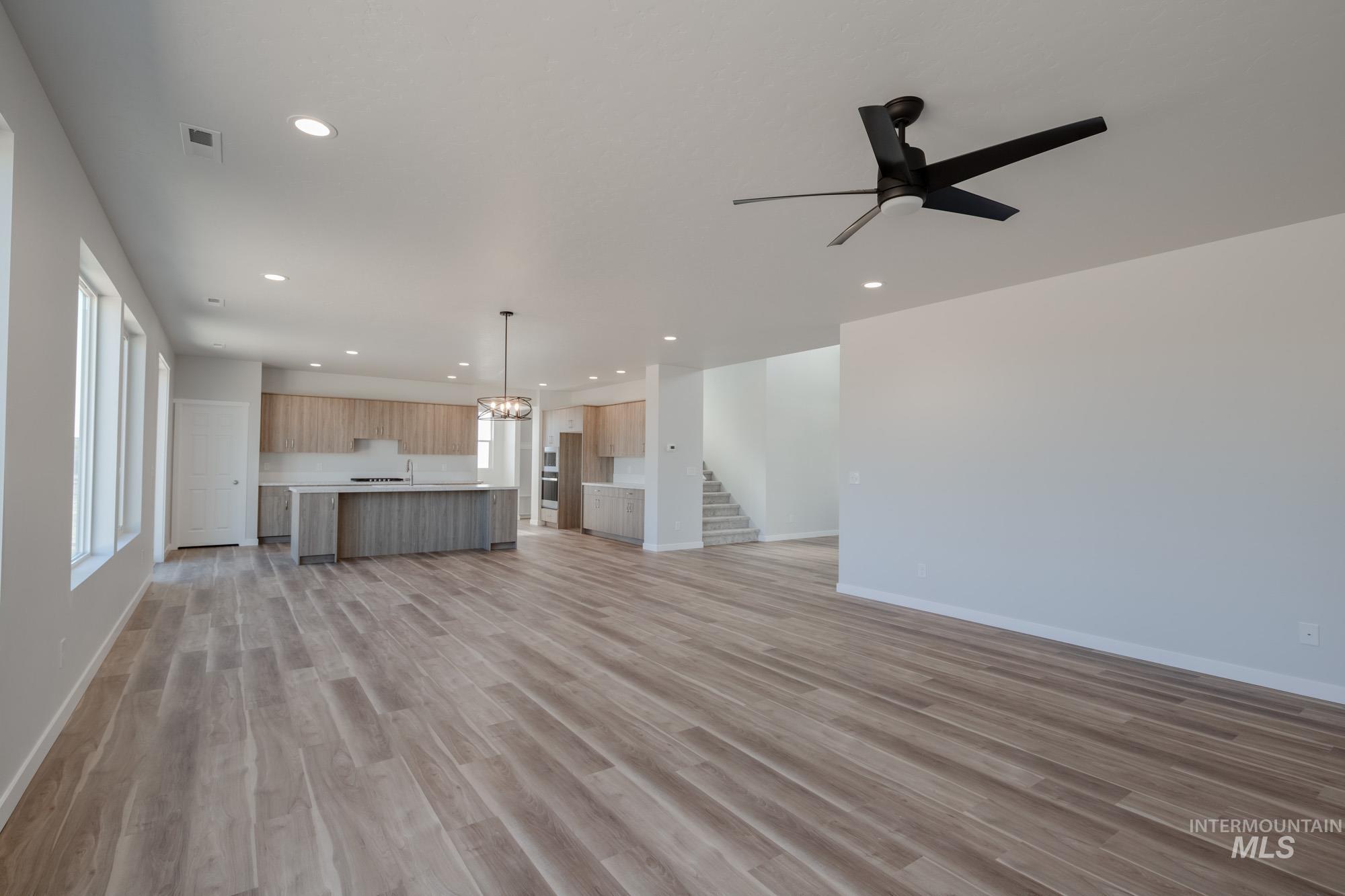 Unfurnished living room featuring a chandelier, light wood-style floors, plenty of natural light, recessed lighting, and ceiling fan