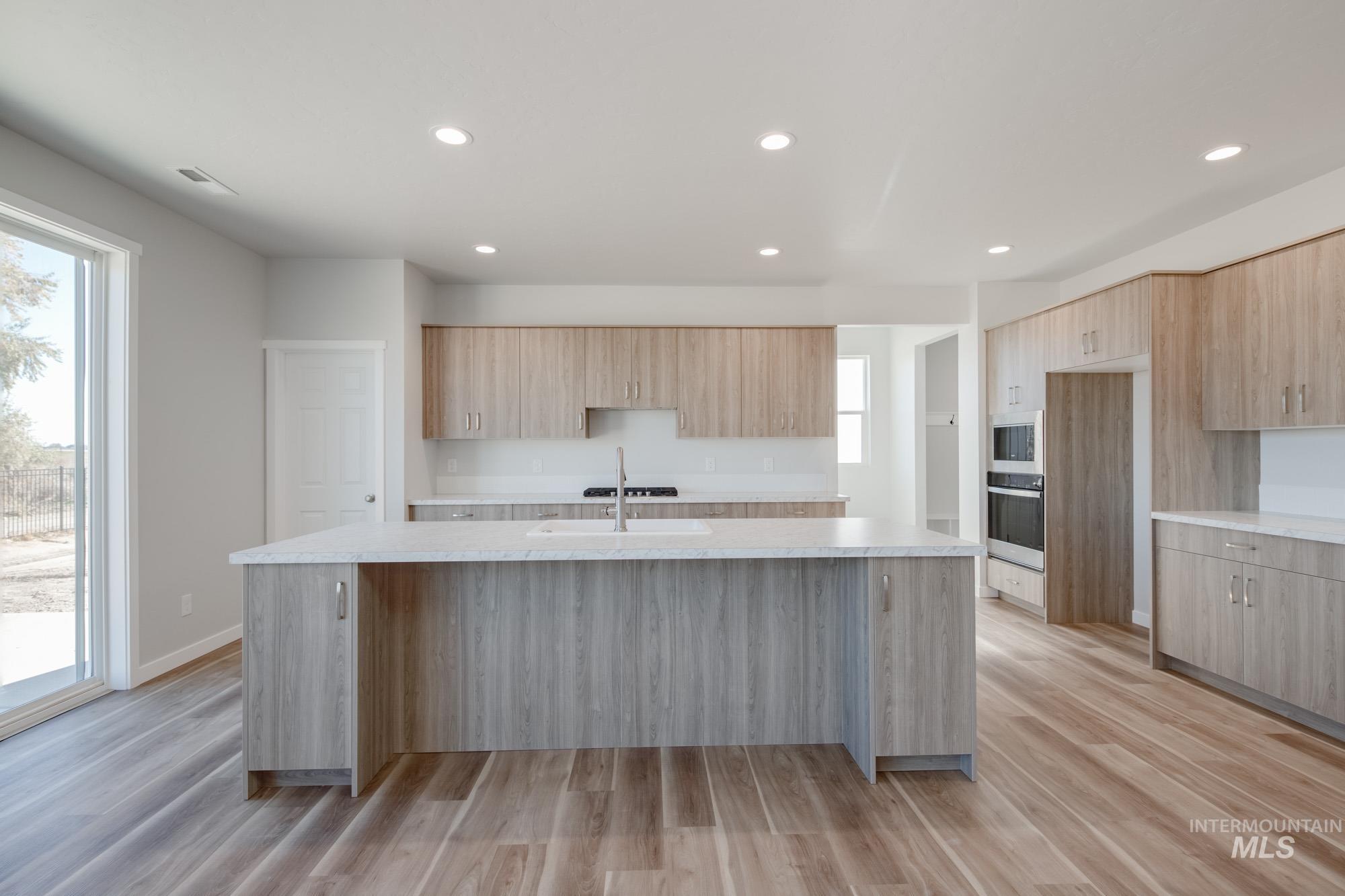 Kitchen with an island with sink, light wood finished floors, recessed lighting, stainless steel appliances, and modern cabinets