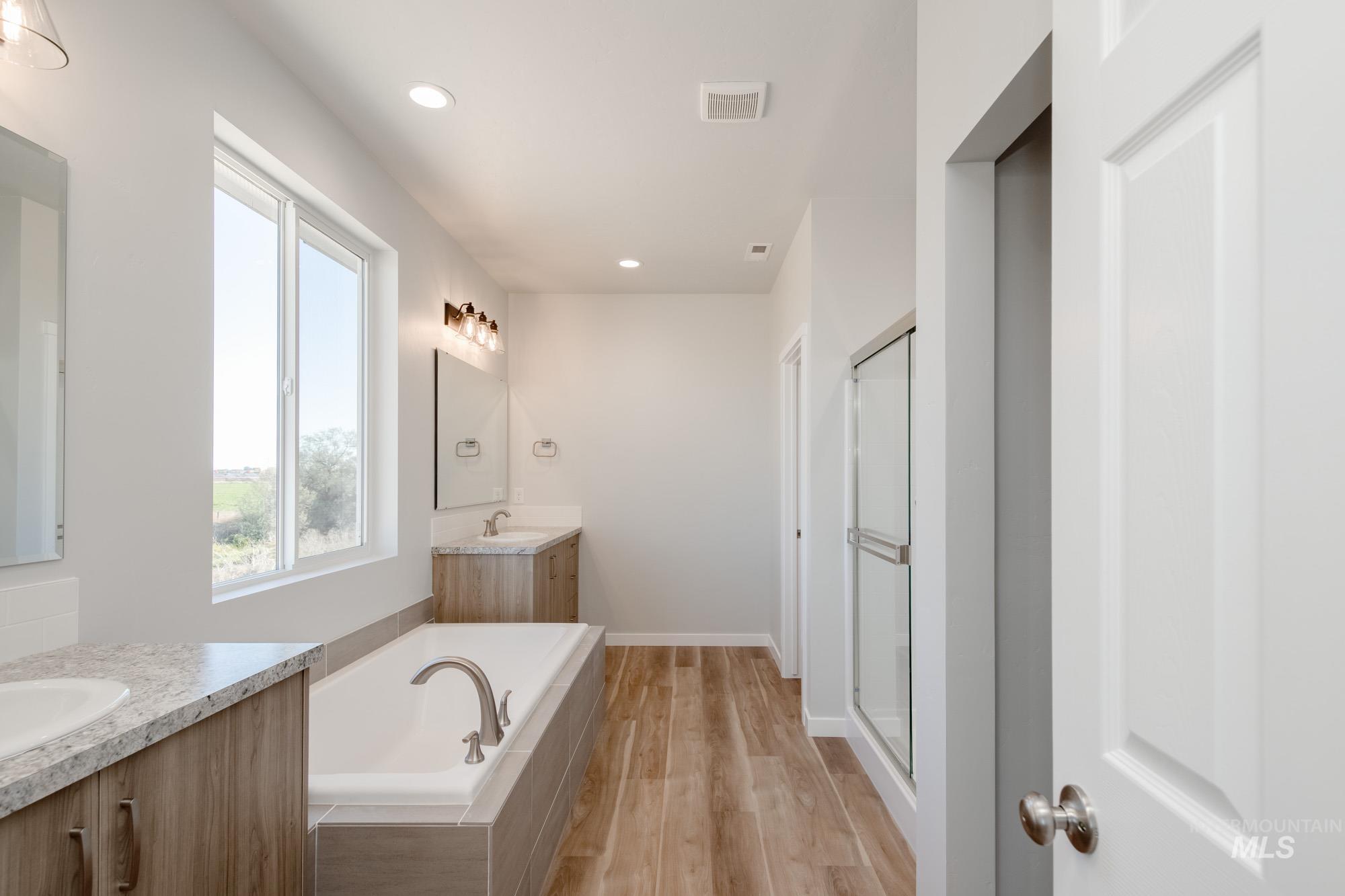 Bathroom with two vanities, a bath, recessed lighting, light wood-style floors, and a shower stall
