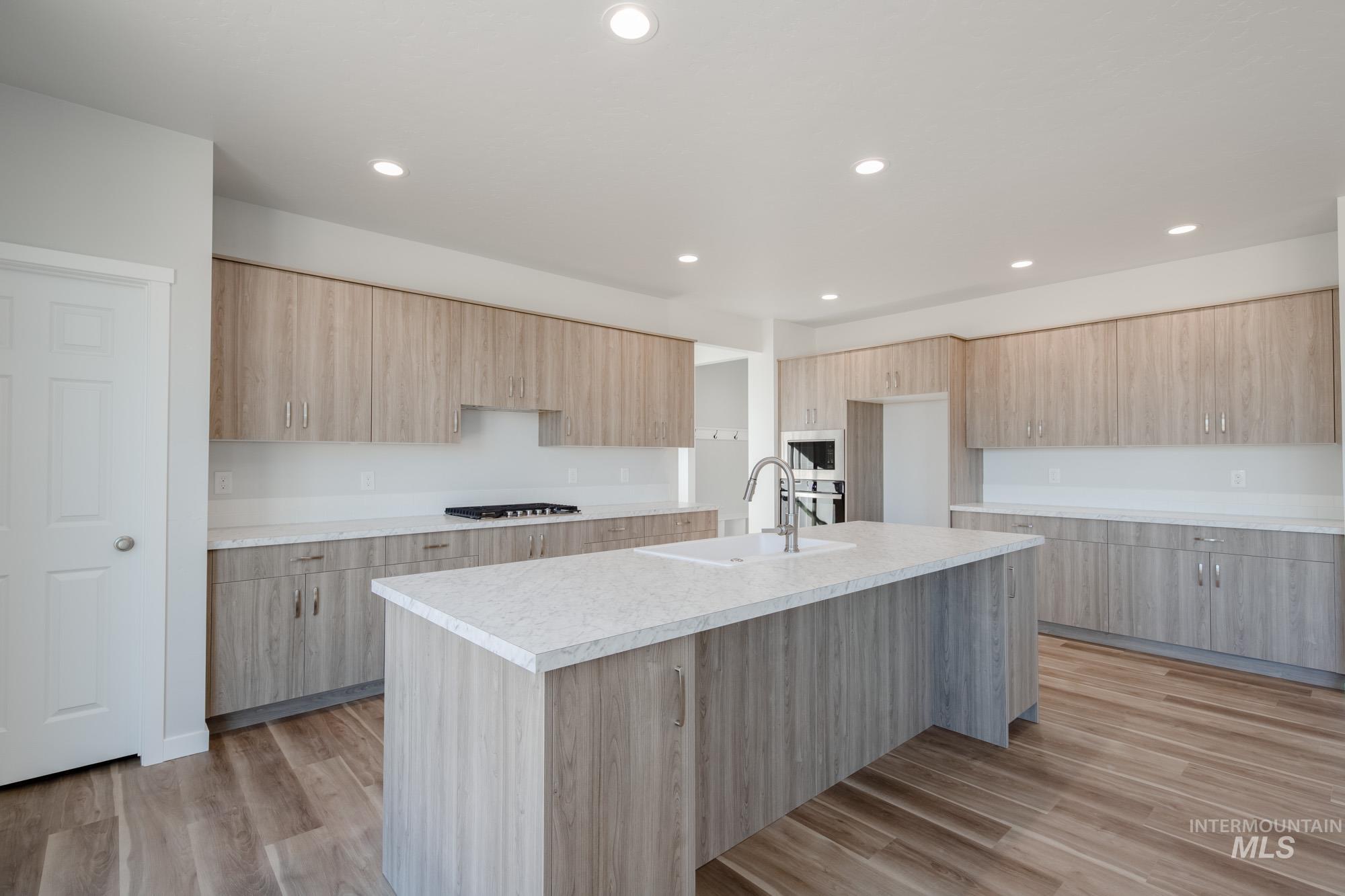 Kitchen with an island with sink, recessed lighting, light countertops, light wood finished floors, and stainless steel appliances