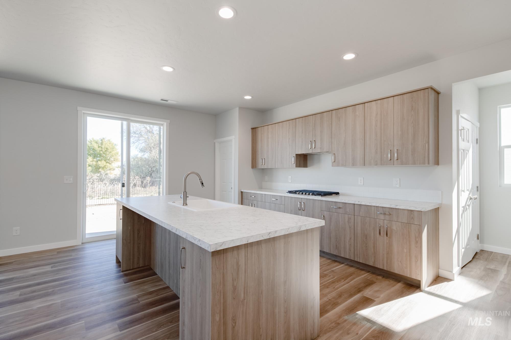 Kitchen featuring light brown cabinets, light countertops, light wood-style floors, a center island with sink, and recessed lighting