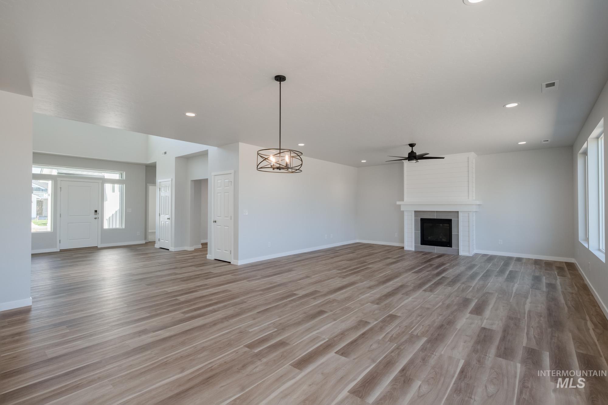 Unfurnished living room with a tiled fireplace, light wood-style flooring, a chandelier, recessed lighting, and ceiling fan