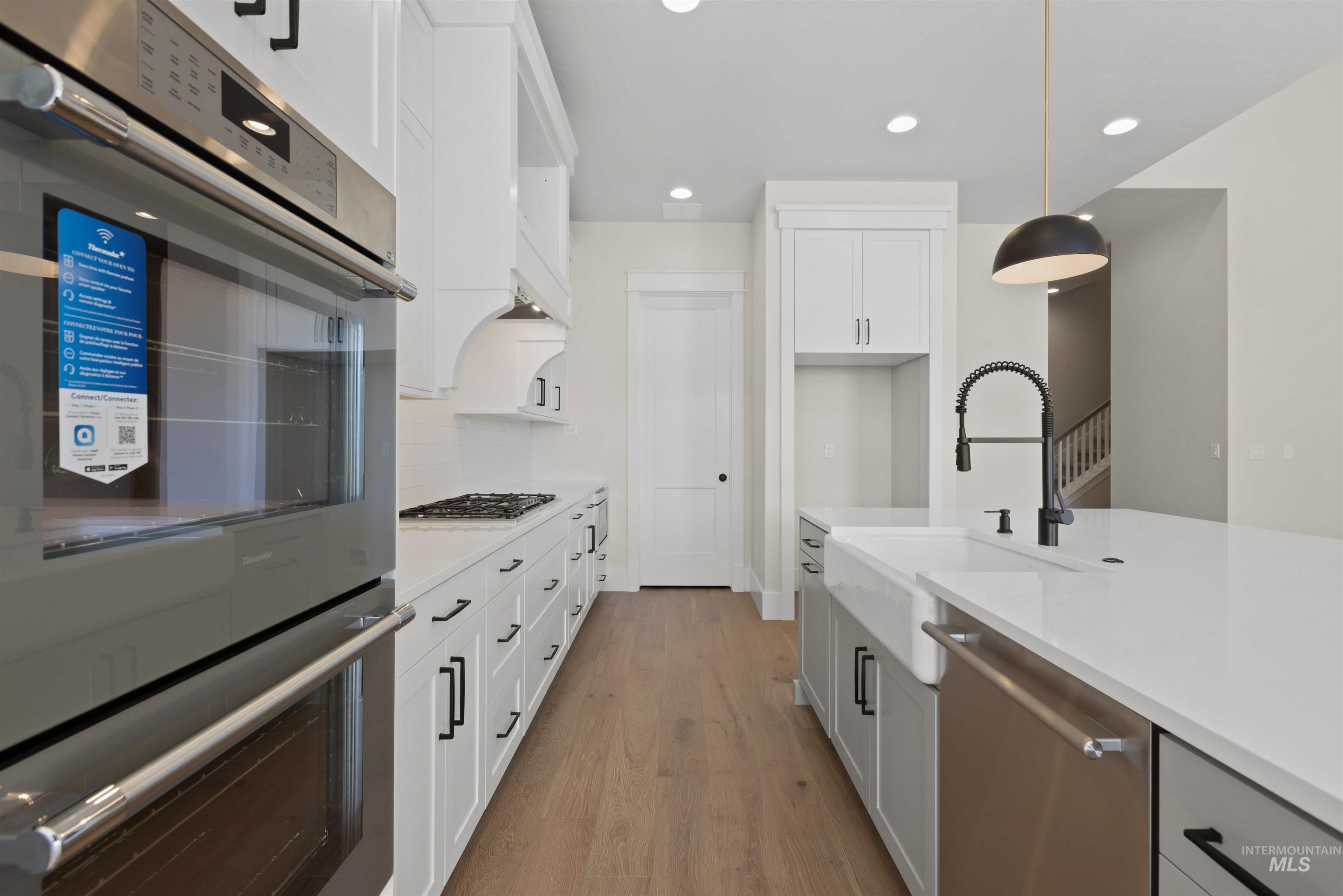 Kitchen featuring stainless steel appliances, light wood-type flooring, hanging light fixtures, light countertops, and white cabinetry