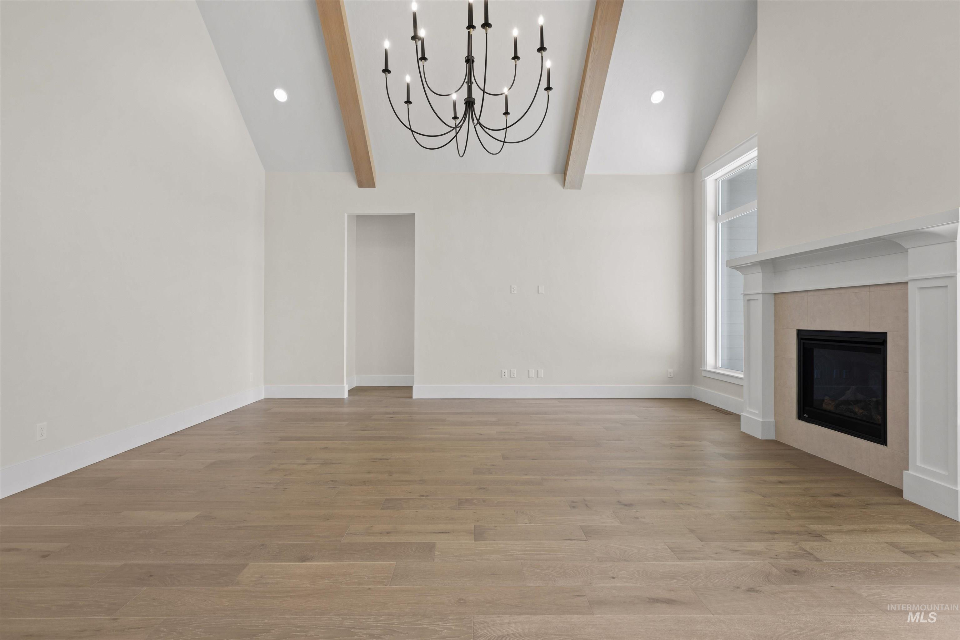 Unfurnished living room with beamed ceiling, a chandelier, high vaulted ceiling, light wood finished floors, and a tiled fireplace