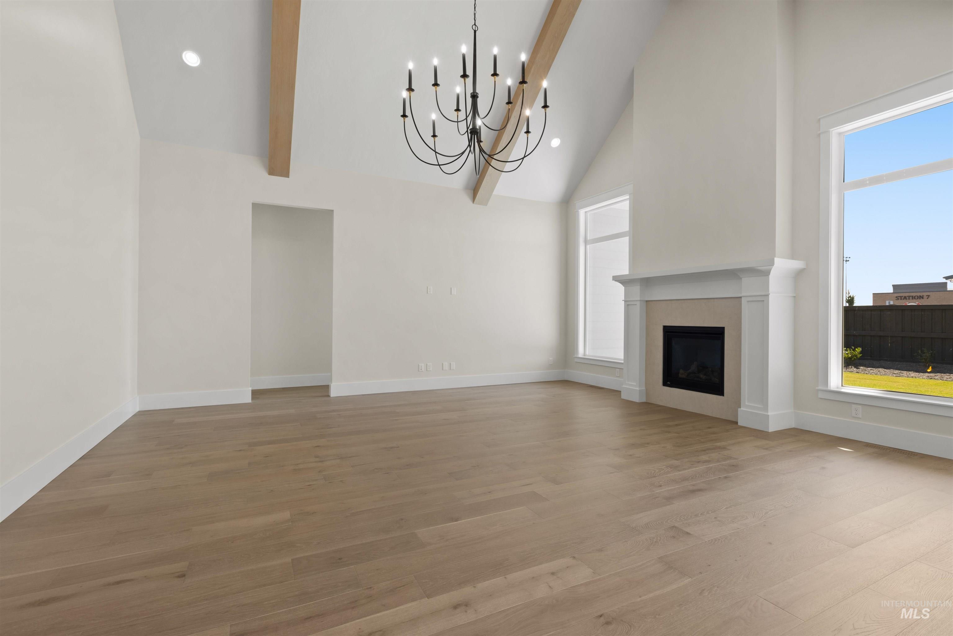 Unfurnished living room featuring high vaulted ceiling, healthy amount of natural light, a chandelier, light wood finished floors, and a fireplace
