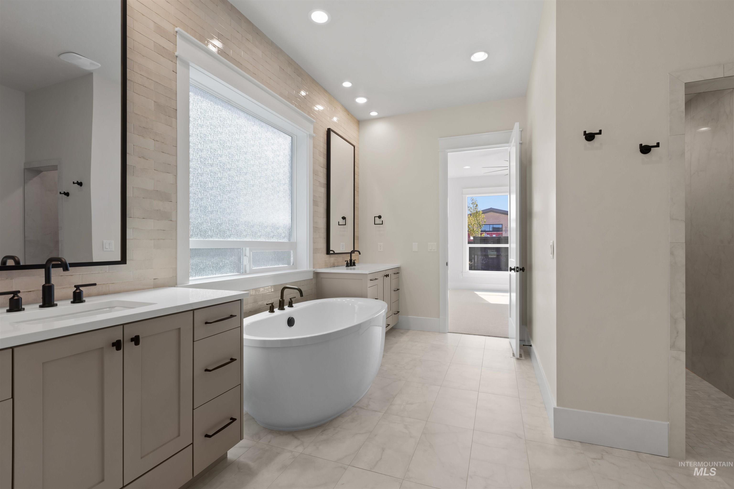 Full bath featuring plenty of natural light, two vanities, a freestanding bath, walk in shower, and recessed lighting