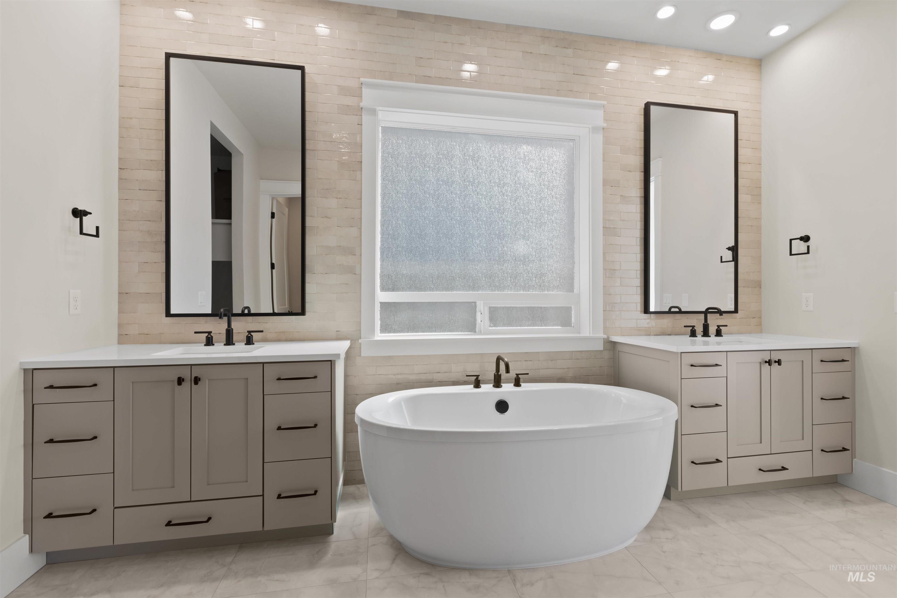 Bathroom with marble look tiles, a freestanding bath, two vanities, recessed lighting, and tile walls