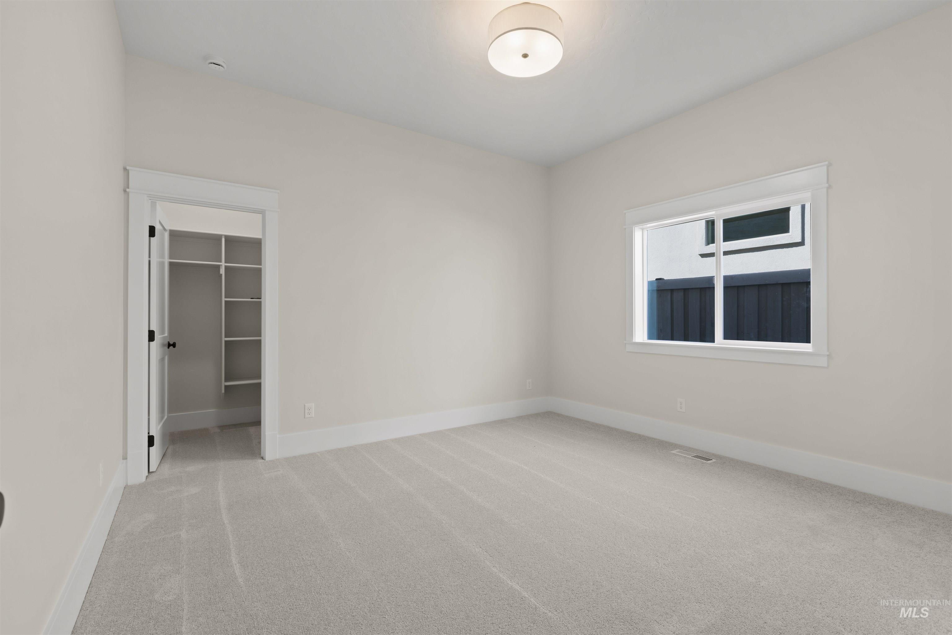 Unfurnished bedroom featuring light carpet and a walk in closet