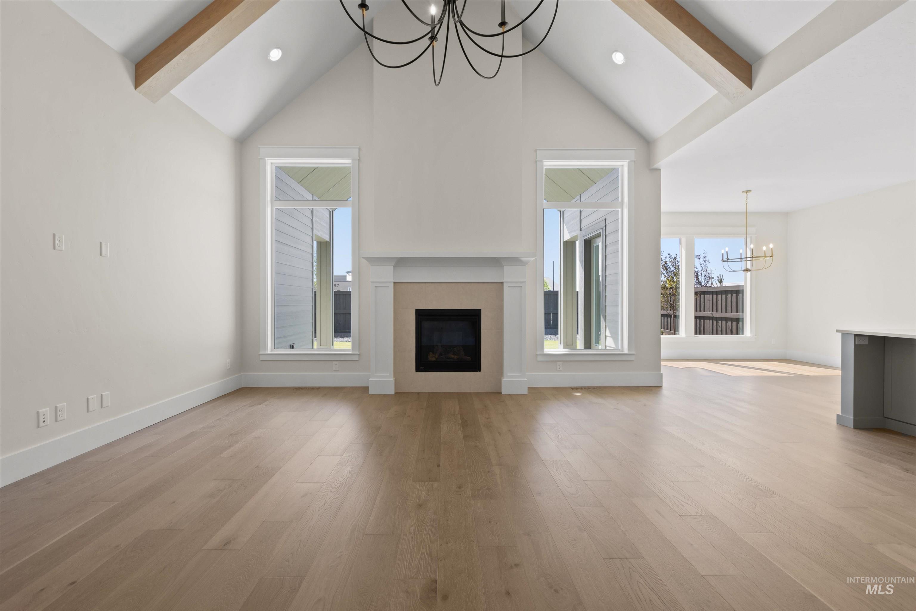 Unfurnished living room featuring a chandelier, beam ceiling, high vaulted ceiling, a fireplace, and light wood-style floors