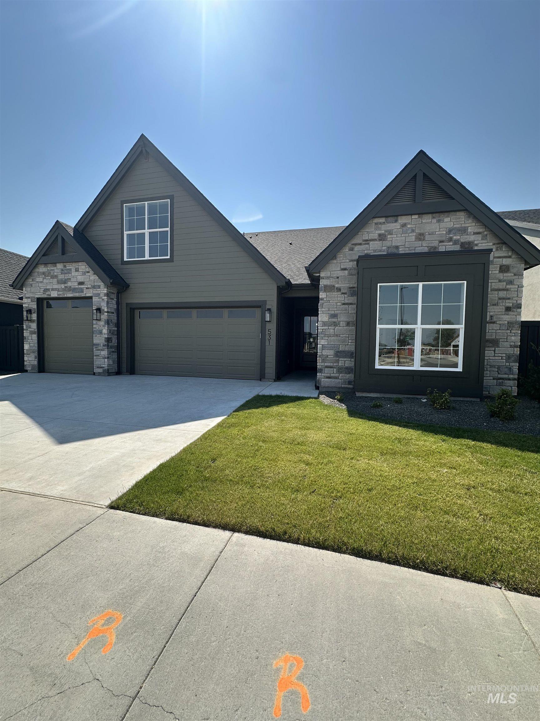 View of front of property featuring stone siding, a front lawn, concrete driveway, and a garage