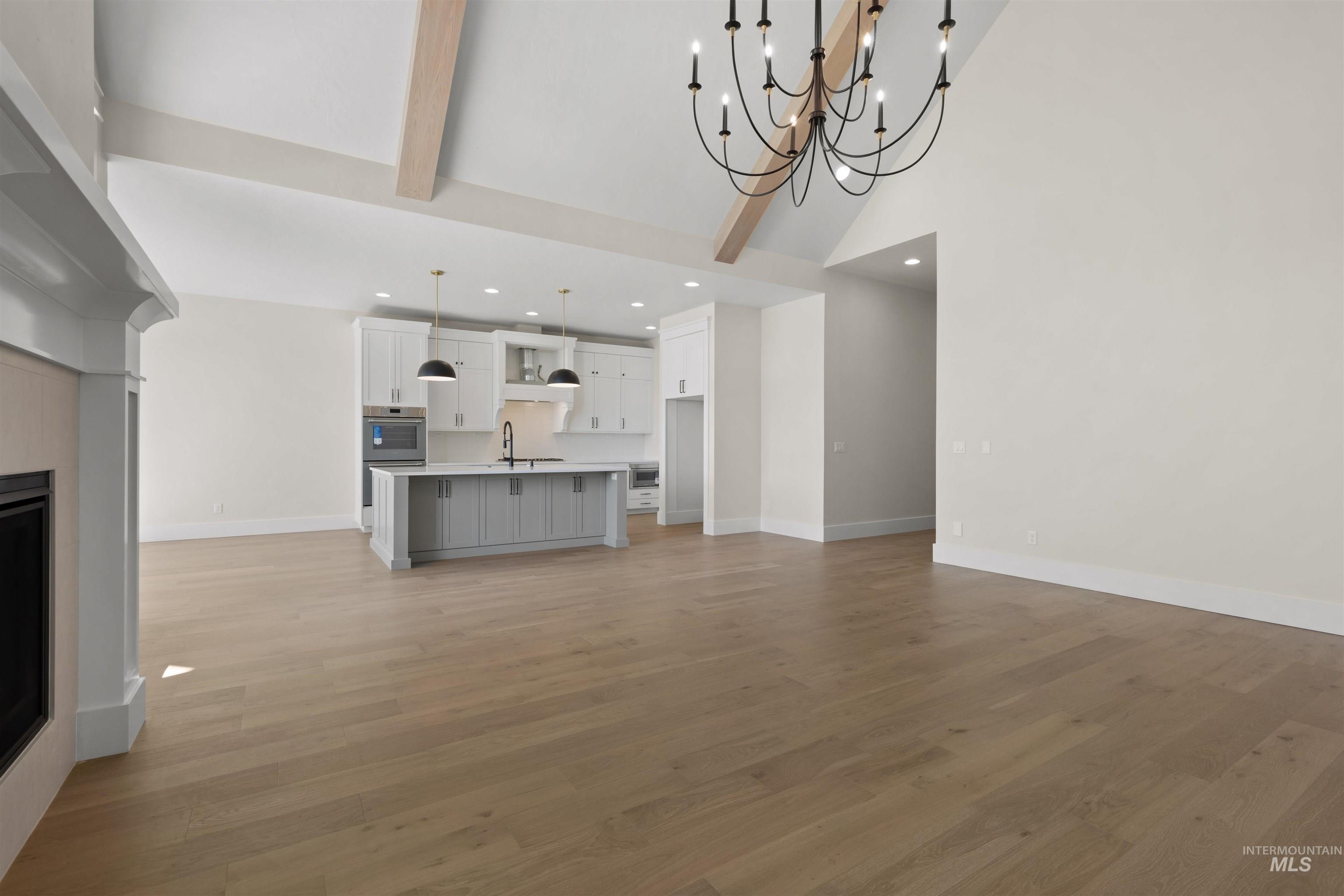 Unfurnished living room featuring high vaulted ceiling, light wood-type flooring, recessed lighting, beam ceiling, and a chandelier