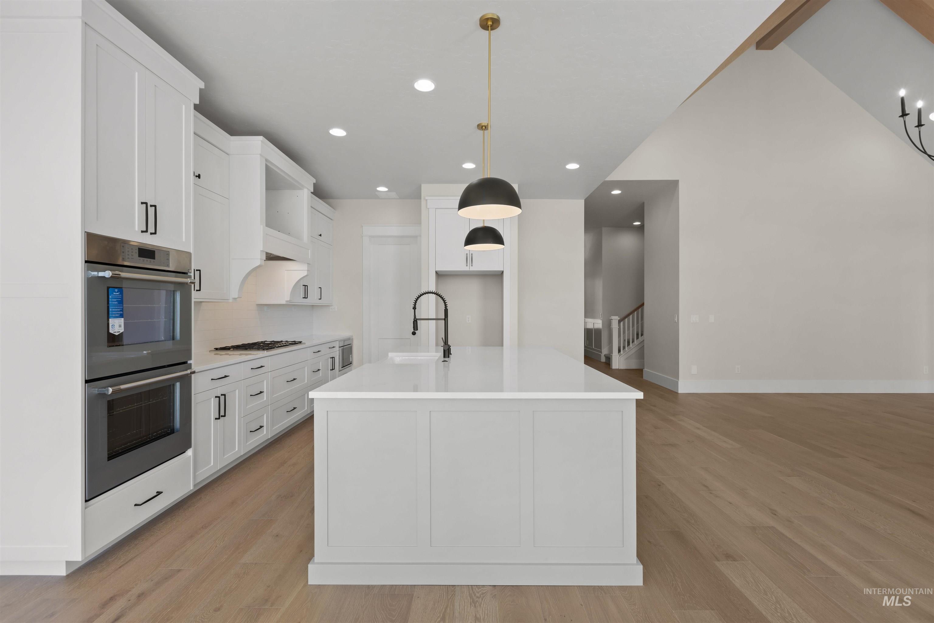 Kitchen featuring appliances with stainless steel finishes, light wood-style flooring, tasteful backsplash, white cabinetry, and recessed lighting
