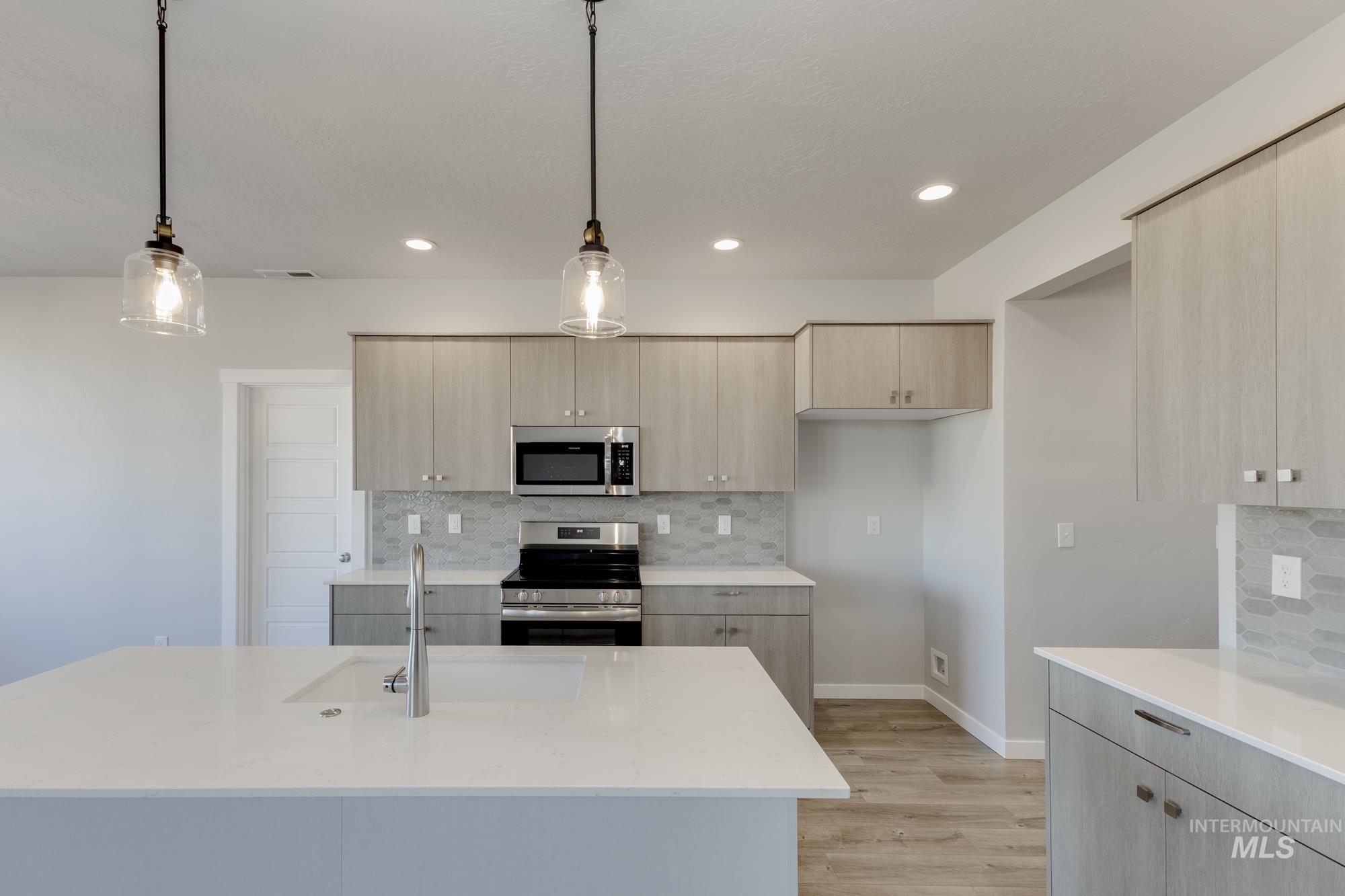 Kitchen with pendant lighting, stainless steel appliances, tasteful backsplash, light stone counters, and light wood-style flooring