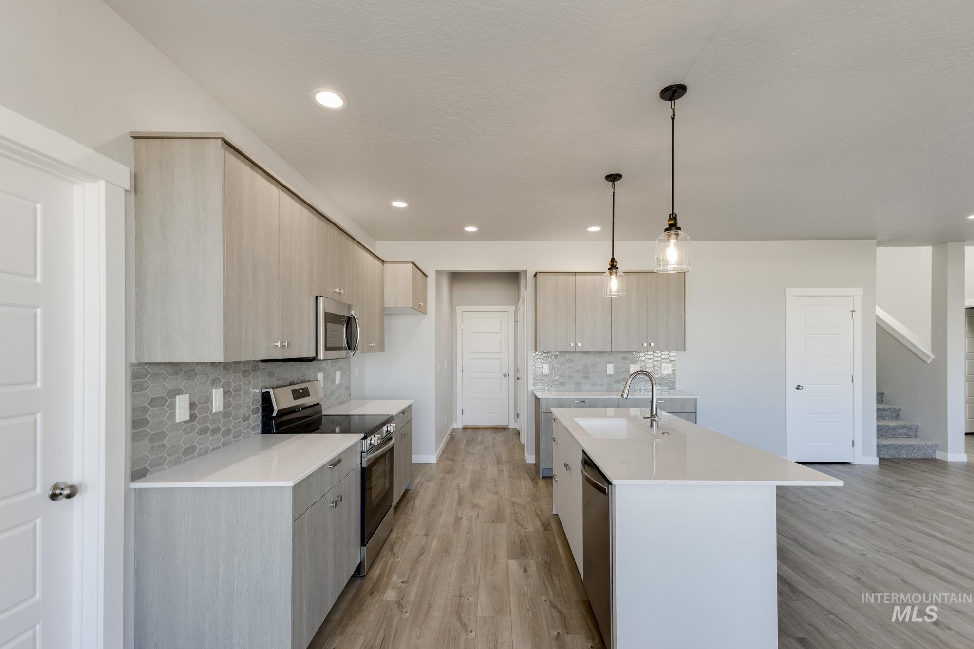 Kitchen featuring modern cabinets, light brown cabinets, appliances with stainless steel finishes, light stone counters, and decorative light fixtures