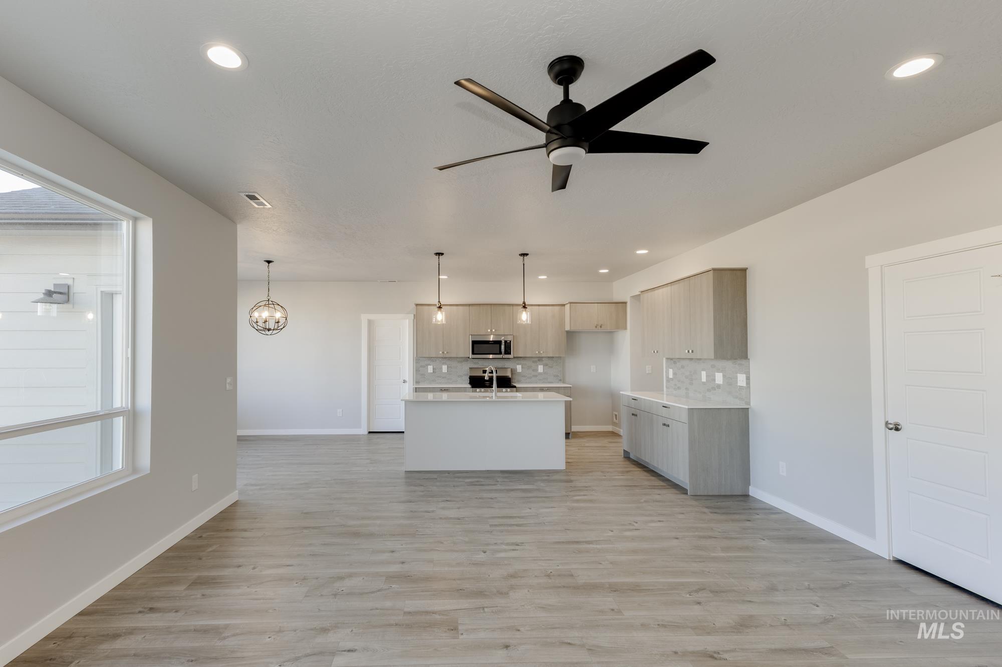 Kitchen with open floor plan, pendant lighting, an island with sink, decorative backsplash, and a chandelier