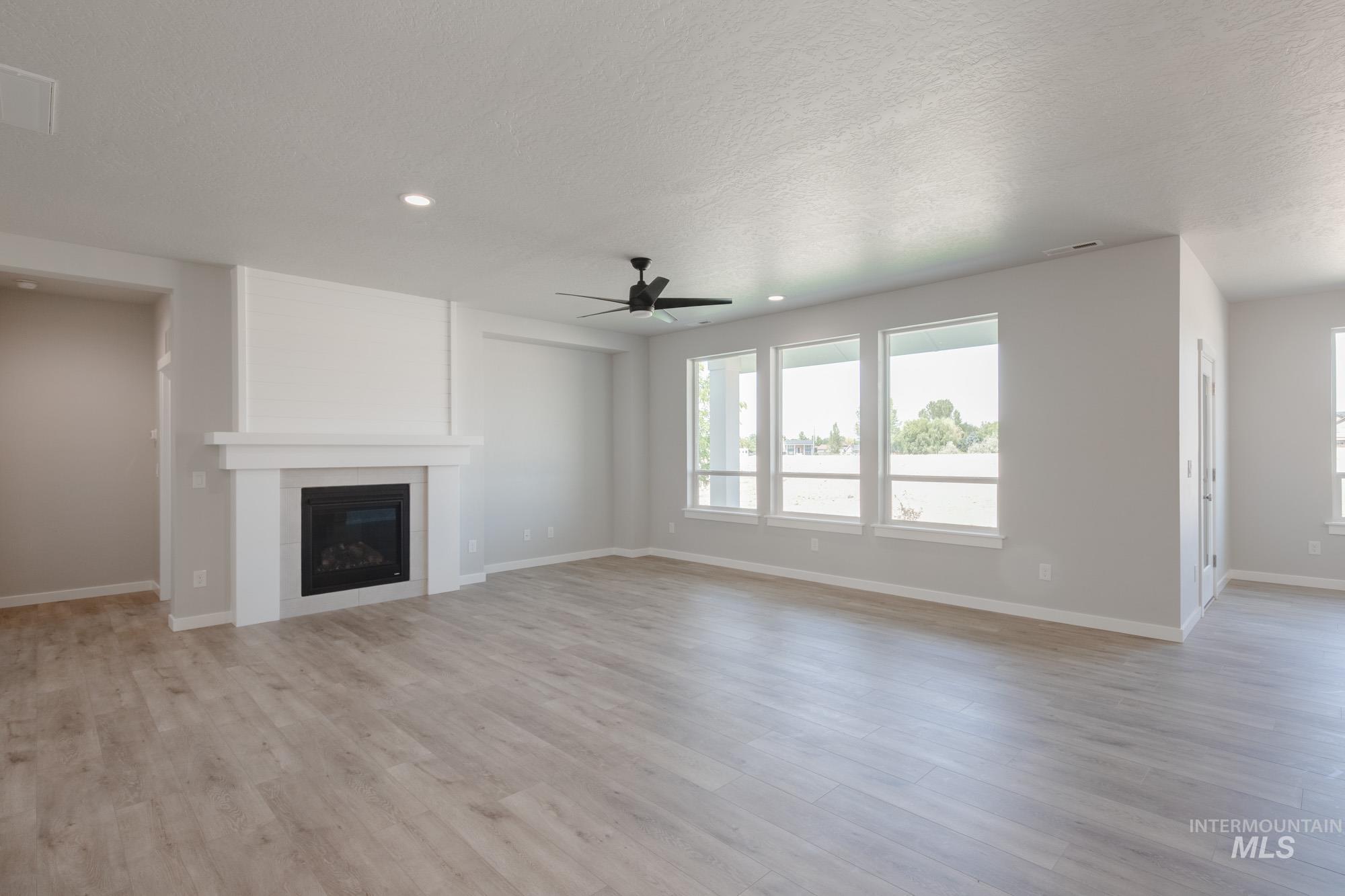 Unfurnished living room with a large fireplace, light wood finished floors, ceiling fan, recessed lighting, and a textured ceiling