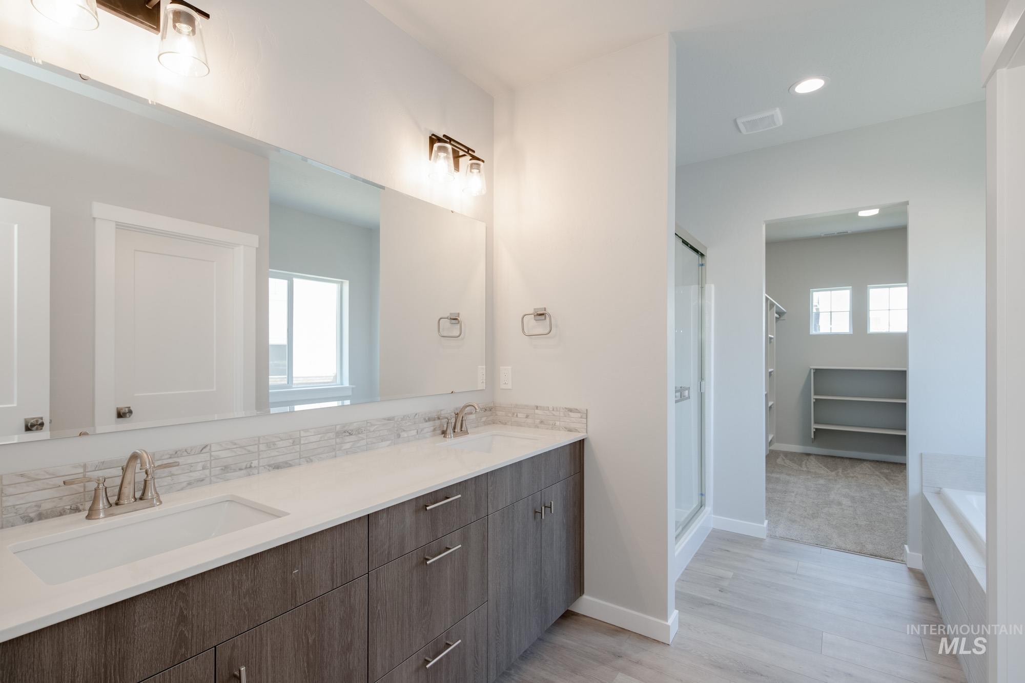 Bathroom featuring a shower stall, double vanity, light wood-style floors, a tub, and a walk in closet