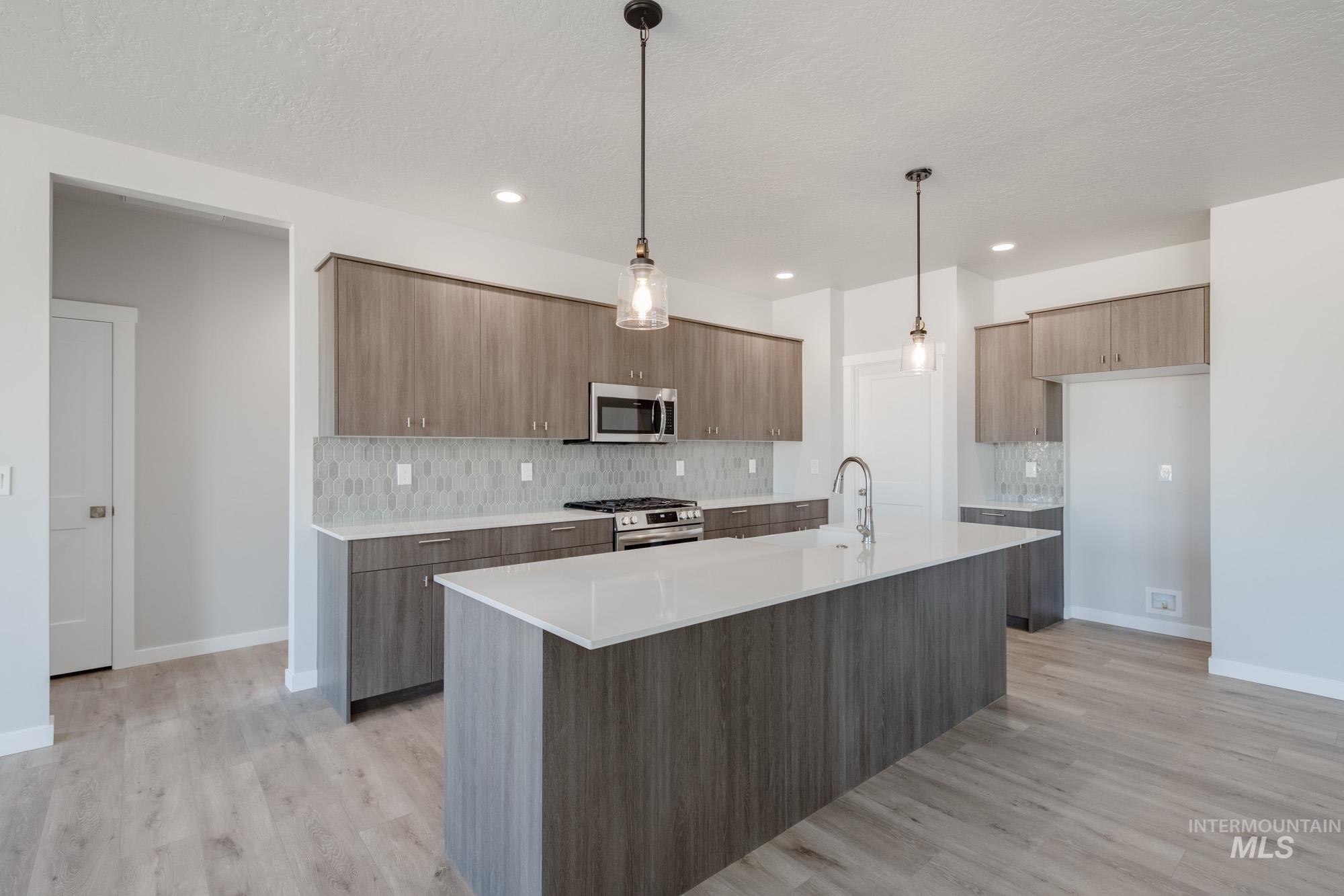 Kitchen with backsplash, modern cabinets, pendant lighting, appliances with stainless steel finishes, and light wood-style floors