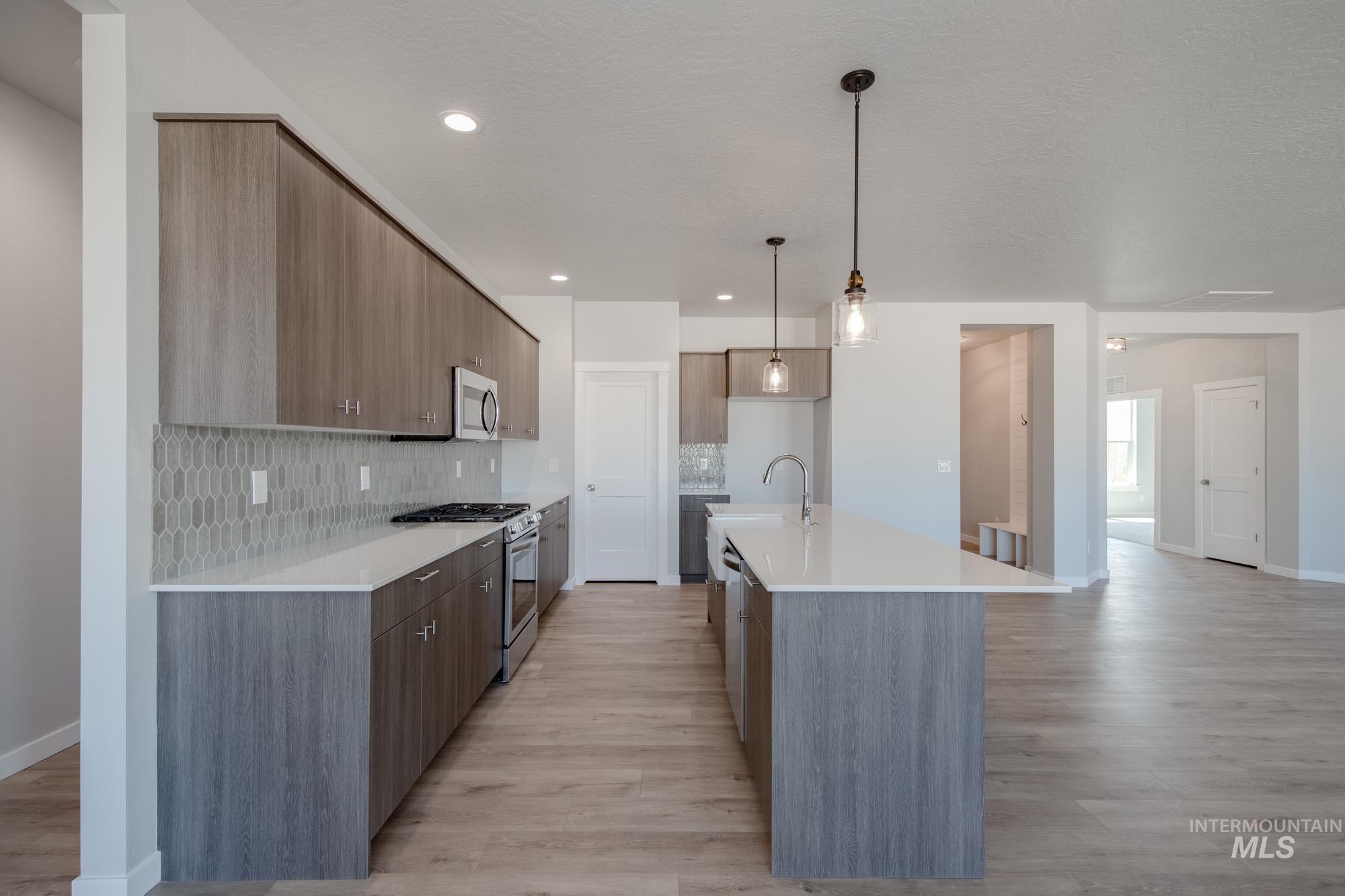 Kitchen featuring decorative light fixtures, appliances with stainless steel finishes, modern cabinets, a kitchen island with sink, and tasteful backsplash