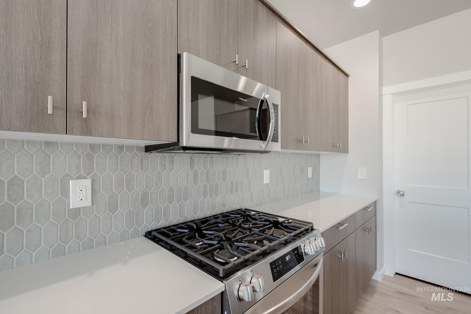 Kitchen featuring appliances with stainless steel finishes, modern cabinets, tasteful backsplash, light wood-style floors, and light stone counters