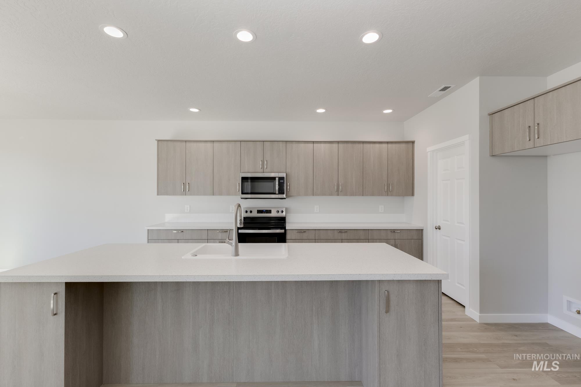 Kitchen featuring appliances with stainless steel finishes, a center island with sink, light brown cabinetry, light wood-style flooring, and modern cabinets
