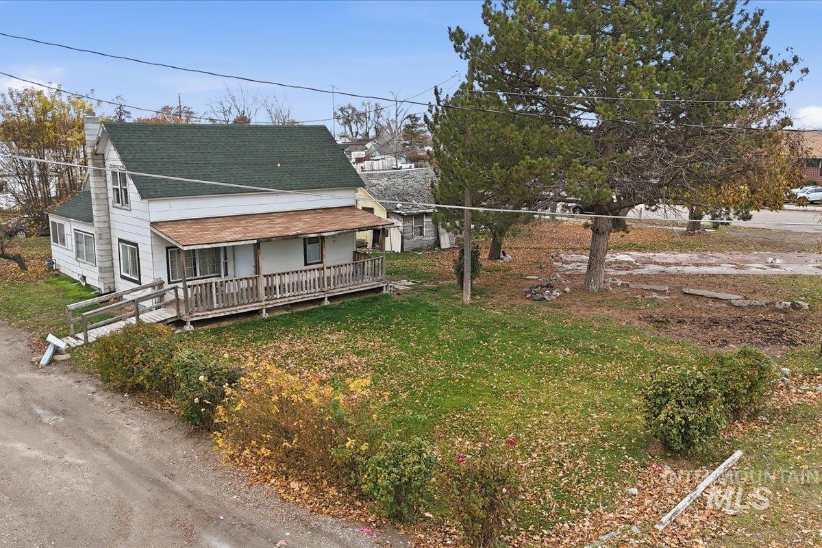 View of front of home with a chimney, a shingled roof, covered porch, and a front lawn