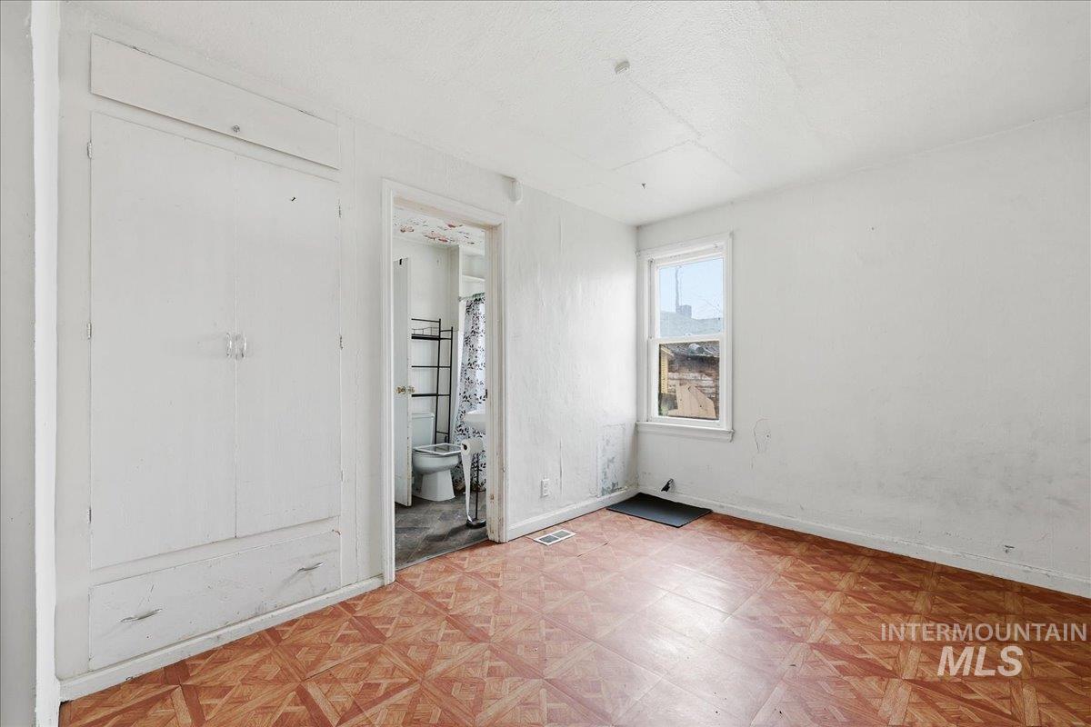 Unfurnished bedroom with light flooring, ensuite bath, and a textured ceiling