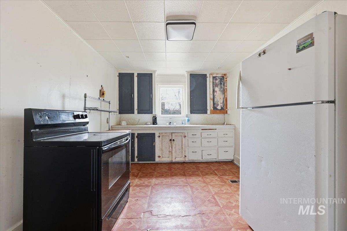 Kitchen with freestanding refrigerator, black range with electric stovetop, and light flooring