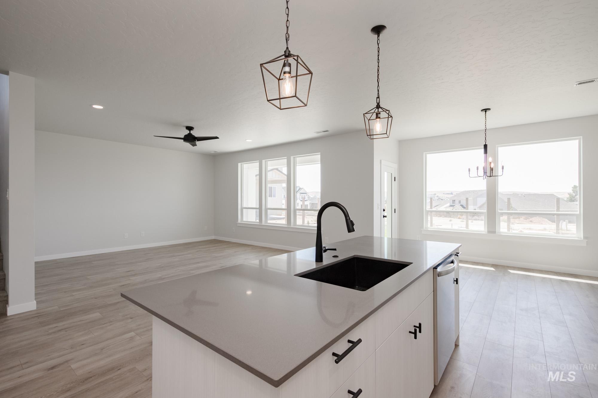 Kitchen with pendant lighting, a kitchen island with sink, light wood-style flooring, white cabinets, and a chandelier