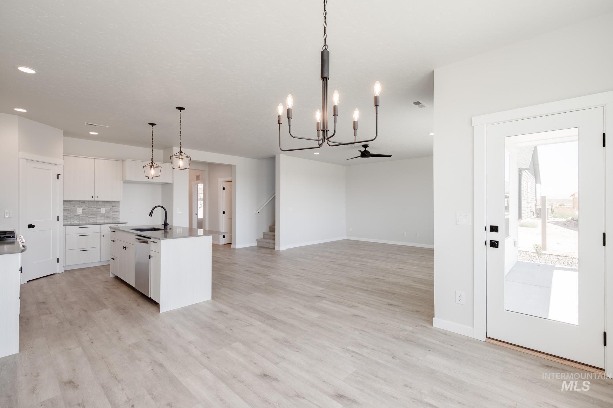 Kitchen with hanging light fixtures, a chandelier, a center island with sink, decorative backsplash, and white cabinets