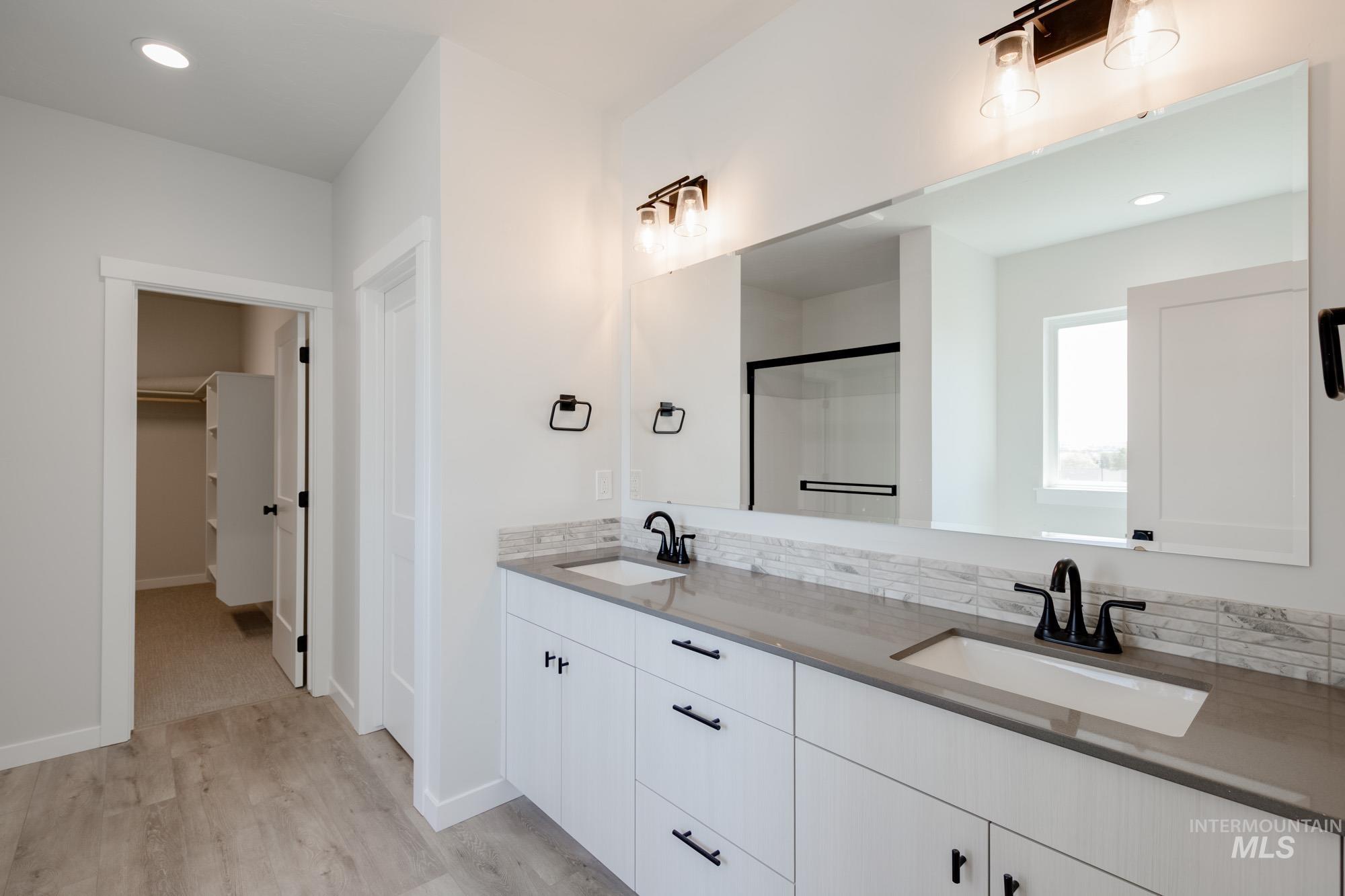 Bathroom with double vanity, recessed lighting, light wood-style flooring, a walk in closet, and tasteful backsplash