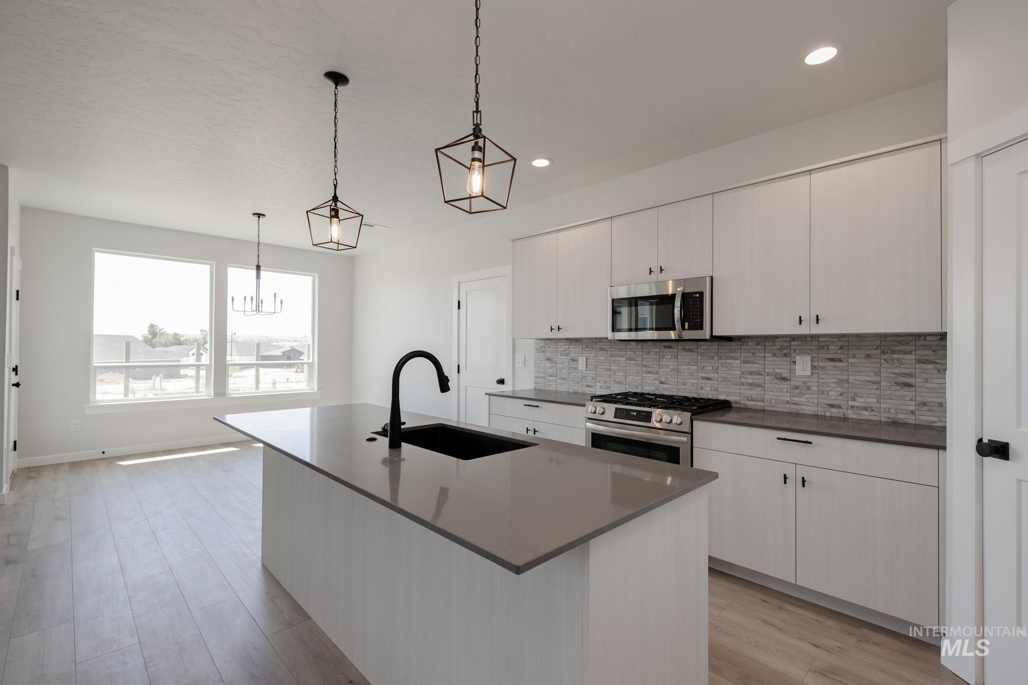 Kitchen featuring appliances with stainless steel finishes, a center island with sink, tasteful backsplash, hanging light fixtures, and light wood-style flooring