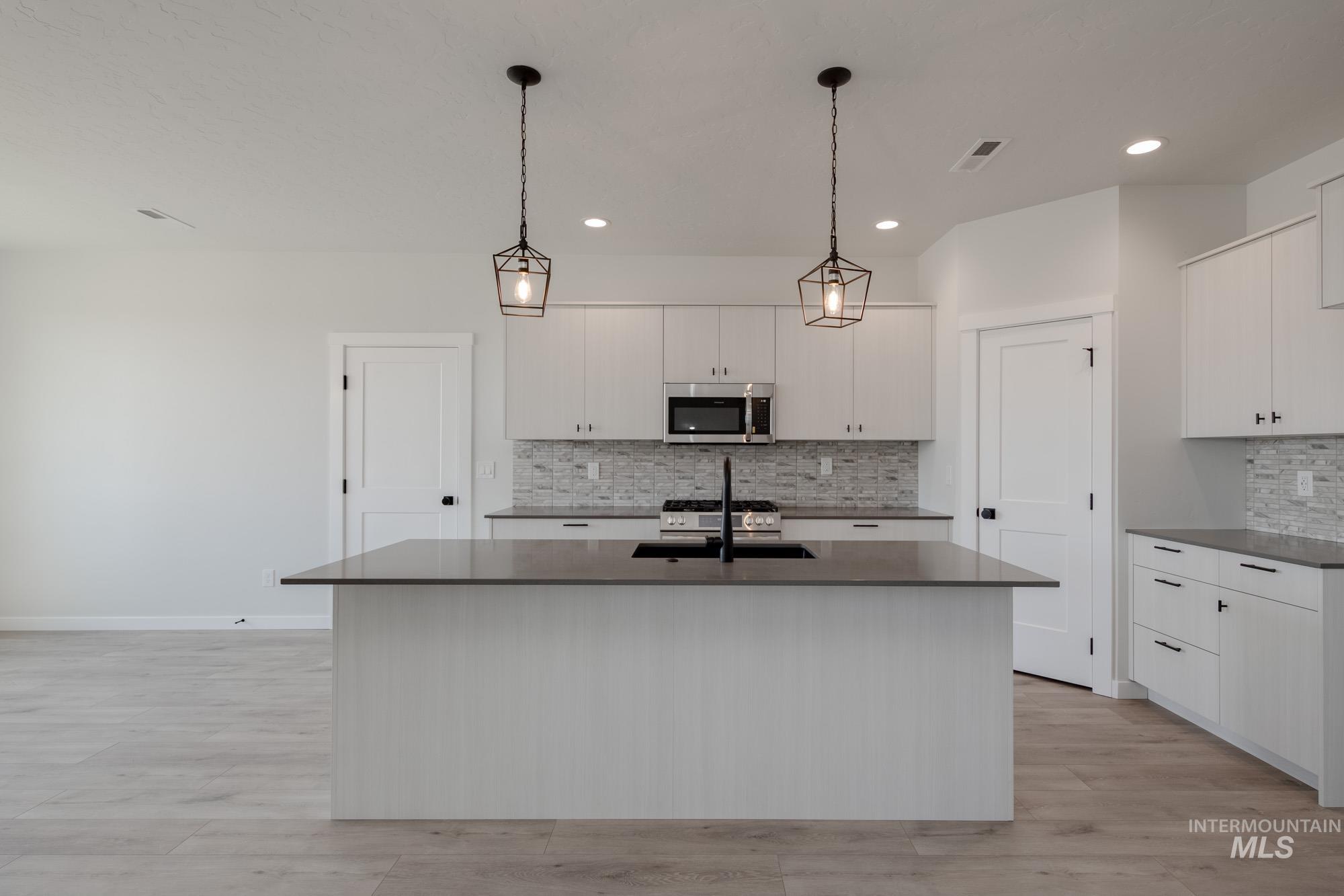 Kitchen with tasteful backsplash, stainless steel appliances, a kitchen island with sink, decorative light fixtures, and white cabinetry